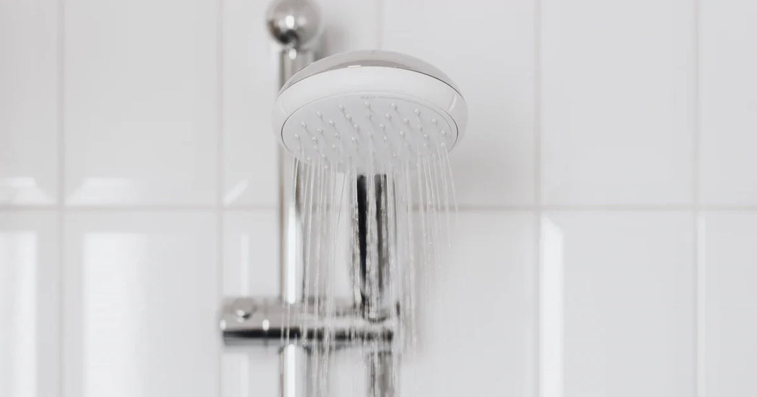 A handheld shower head running against clean white bathroom tile.