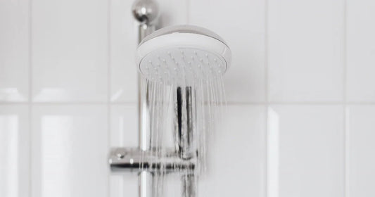 A handheld shower head running against clean white bathroom tile.