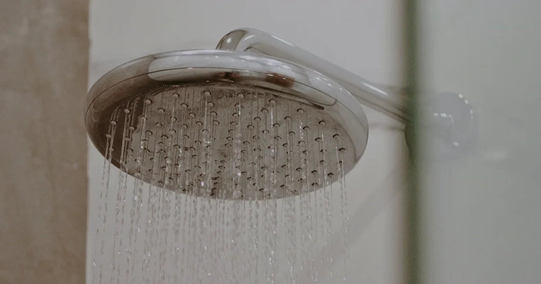 Water running from a chrome shower head while the surrounding connections remain visible for leak inspection.